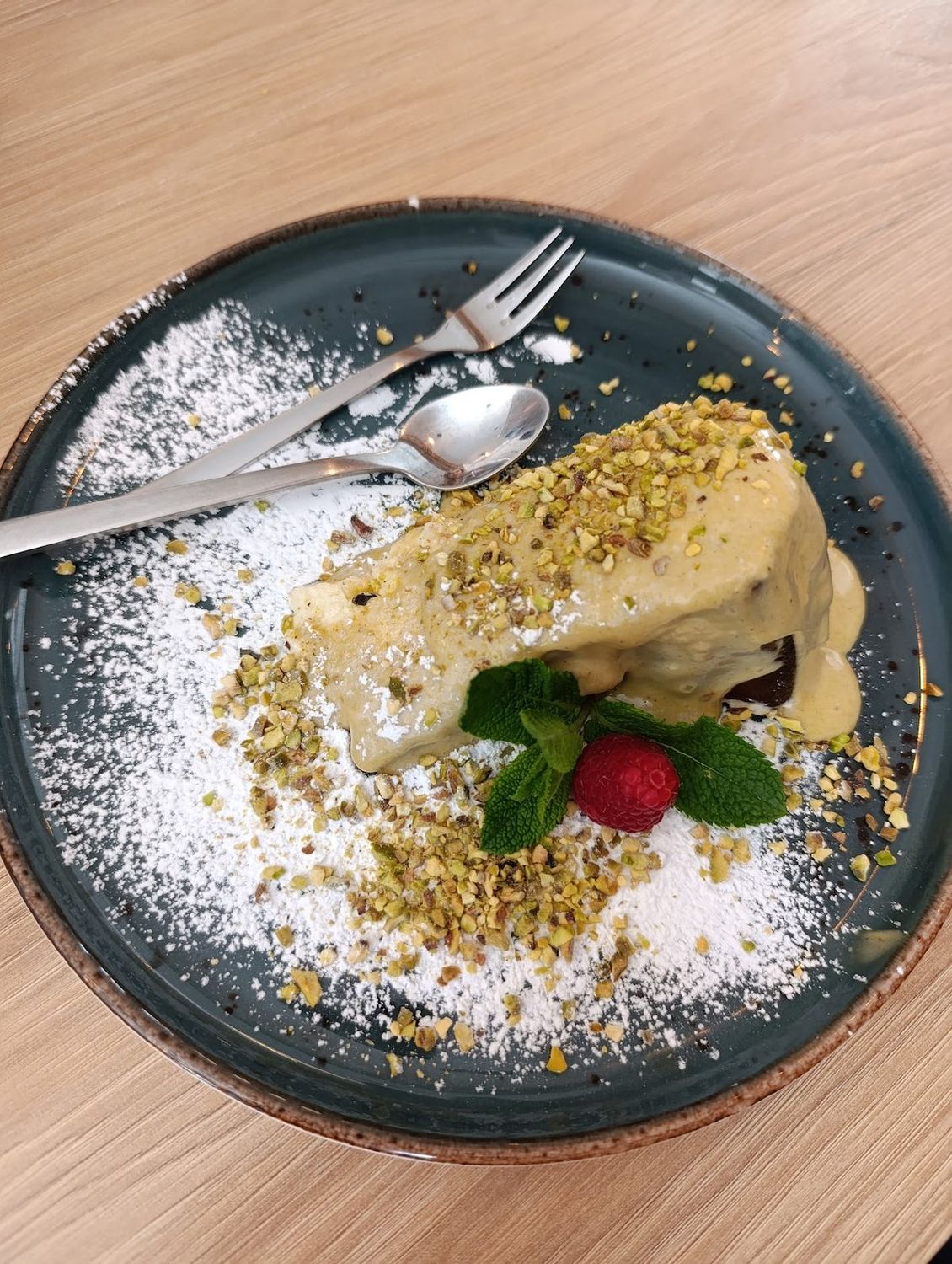 Deser z polewą pistacjową, malinami i miętą na ciemnym talerzu