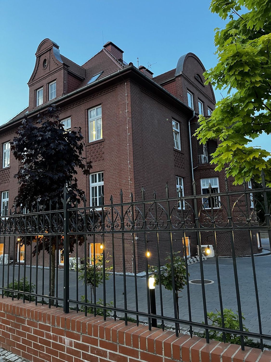 Ceglana kamienica Bon Żur w Brzegu o zmierzchu, rozświetlone okna i podjazd
